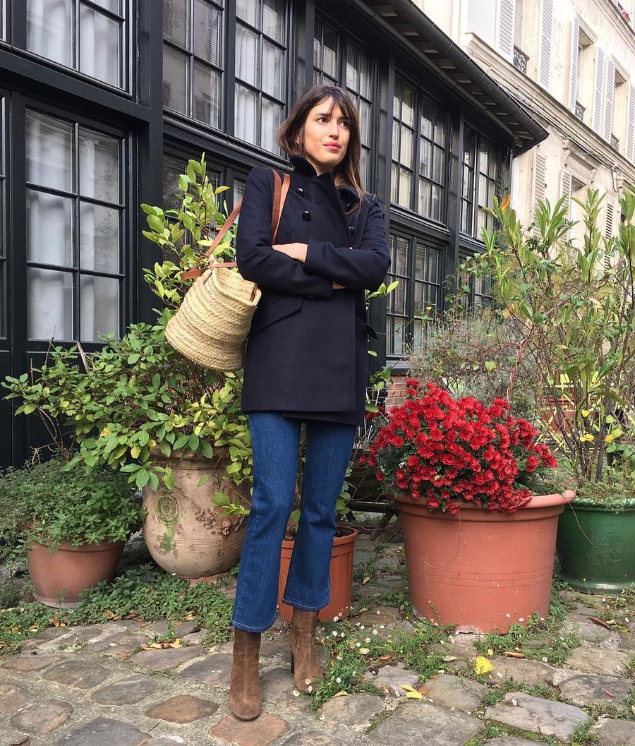 Jeanne Damas wearing a navy coat with suede boots and a straw tote bag